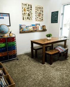 a room with a table, bookshelf and several pictures on the wall