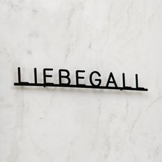 the word liebegail is written in black on a white marble wall with a metal bar