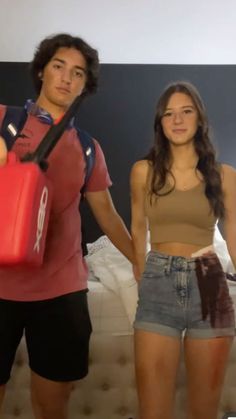 a man and woman standing next to each other in front of a bed holding luggage