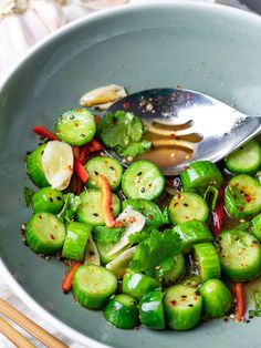 a bowl filled with sliced up green vegetables and a spoon in it next to chopsticks