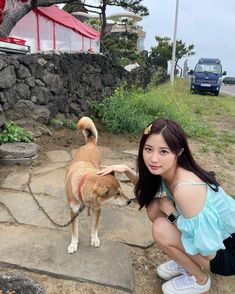 a woman kneeling down petting a dog on top of a stone walkway next to a rock wall