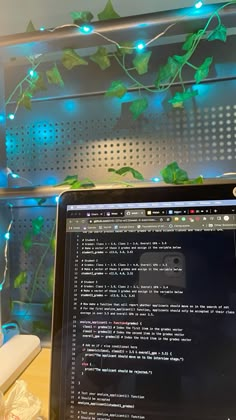 a laptop computer sitting on top of a wooden desk next to a plant covered wall