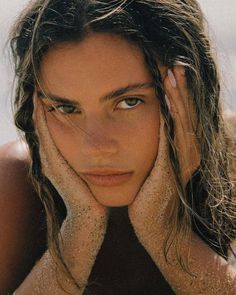 a beautiful young woman laying on top of a sandy beach next to the ocean with her hands under her face