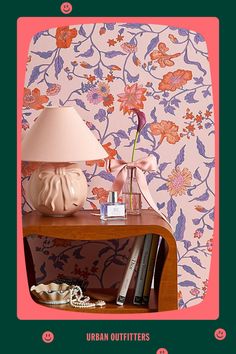 a pink lamp sitting on top of a wooden table next to a wallpapered wall