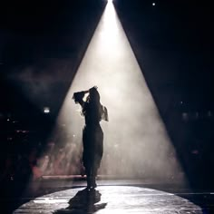 a woman standing in the dark with her hands on her head and light coming from behind her