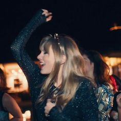 two young women are dancing together in the dark at an outdoor event, one is holding her arms up