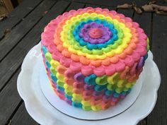 a multicolored cake sitting on top of a white plate next to a wooden table