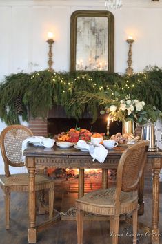 a dining room table set for two with christmas decorations on the mantel above it