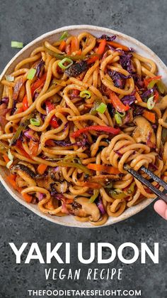 a hand holding a fork over a bowl of noodles with vegetables and sauce on the side