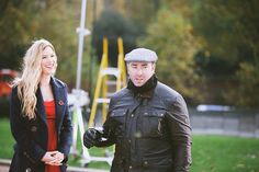 a man and woman standing next to each other in front of a playground area with swings