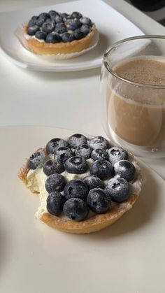 two pastries with blueberries and cream on them next to a cup of coffee