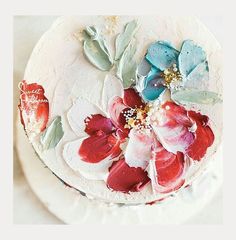 a white cake with red and blue flowers on it's icing, sitting on a plate