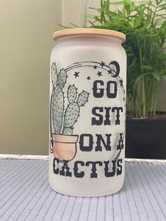 a glass jar that says go sit on a cactus next to a potted plant