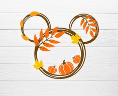 a mickey mouse head with leaves and pumpkins on it's ears, in front of a white wood background