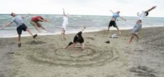 a group of people jumping up in the air on a sandy beach near the ocean