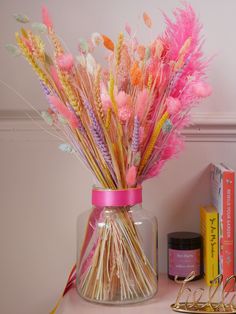 a vase filled with lots of pink and yellow feathers on top of a table next to books