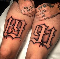 two men with tattoos on their legs sitting next to each other, both holding hands together