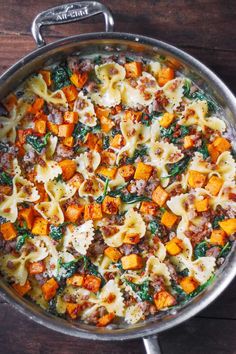 a pan filled with pasta and vegetables on top of a wooden table