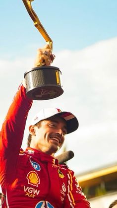 a man holding up a trophy while wearing a red suit and hat on top of his head