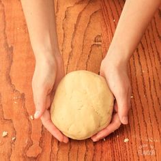 a person holding a ball of bread on top of a wooden table with their hands