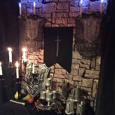 a table with candles and other items in front of a stone wall that has a cross on it