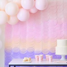 a table topped with cake and cupcakes next to a wall covered in balloons