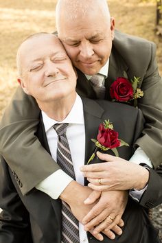 an older man in a suit and tie hugging another old man with roses on his lapel