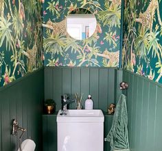 a bathroom with green walls and wallpaper has a white toilet, sink, and mirror