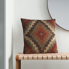 a brown and red pillow sitting on top of a wooden bench next to a mirror