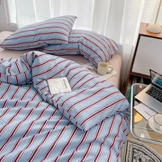 a laptop computer sitting on top of a bed covered in blue and red striped sheets