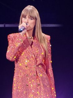 taylor swift performing on stage with microphone in her hand and wearing a bright pink dress