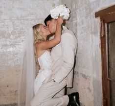 a bride and groom kissing in front of a stone wall with flowers on their head