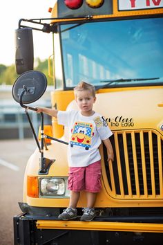 a little boy standing on the front of a school bus with his hand on the handle