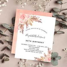 a pink and white floral birthday party card with greenery on the table next to it