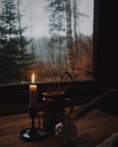 a candle is sitting on a table next to a glass vase with some plants in it