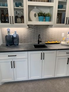 a kitchen with white cabinets and black counter tops, gray tile backsplashes