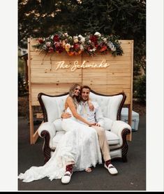 a man and woman sitting on a couch in front of a wooden sign that says the wedding