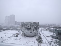 an aerial view of a building with snow on the ground and buildings in the background