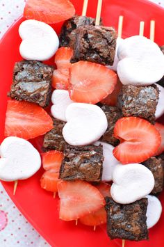 strawberries and marshmallows are on skewers on a red plate