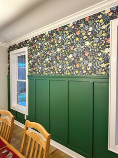 a dining room with green paneling and floral wallpaper on the walls, along with wooden chairs