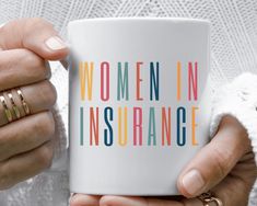 a woman holding a white coffee mug with the words women in academy on it and two gold rings