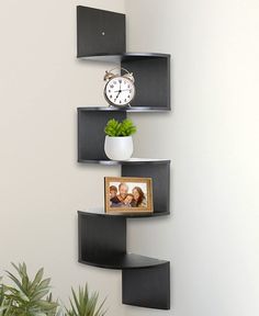 a corner shelf with a clock, plant and picture on it next to a potted plant