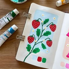 an open book with strawberries and flowers painted on the pages, next to some markers