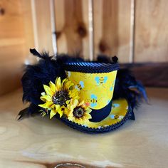 Top off your bee themed mannequin, wreath or shop display with this amazing Bumblebee Mini Top Hat! This little beauty is made of a sturdy yet flexible CVA foam base, covered with coordinating fabrics and trim. The sunflower embellishment and black feathers finish off the hat in style. This is made to order so please allow time for creating and shipping. The sunflowers may vary slightly depending on availability but be assured that they will be of equal or greater quality. Please note in comments if you would like elastic attached and if so state your preference of black or white. Yellow Top Hat, Whimsical Handmade Yellow Hat, Whimsical Yellow Handmade Hat, Whimsical Black Mini Hats For Halloween, Mini Top Hat Headband, Bee Costume, Mini Top Hat, Afternoon Tea Parties, Black Feathers