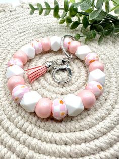 a pink and white beaded bracelet with tassels on it next to a plant