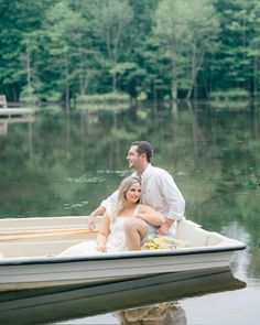 a man and woman are sitting in a small boat on the water with trees in the background