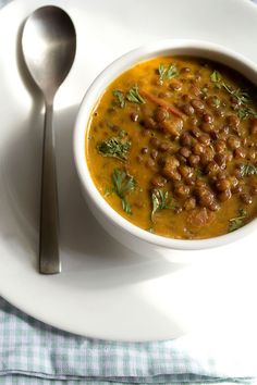 a white plate topped with a bowl of beans and carrots next to a spoon