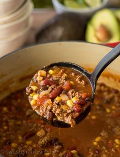 a ladle full of chili and corn is being held up by a wooden spoon