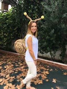 a woman in white shirt standing next to trees with leaves on the ground and wearing antlers