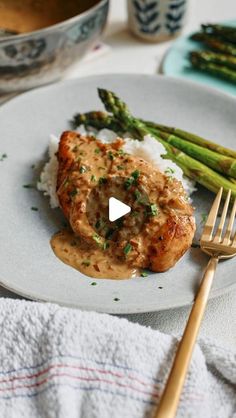 chicken with gravy and asparagus on a plate next to a fork